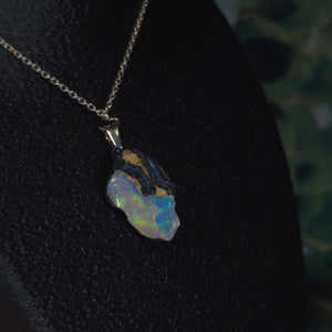 Raw uncut Ethiopian Welo opal pendant. Colour: blue, teal, with green hints, moderate. Body: light blue. Worn on a black display bust.