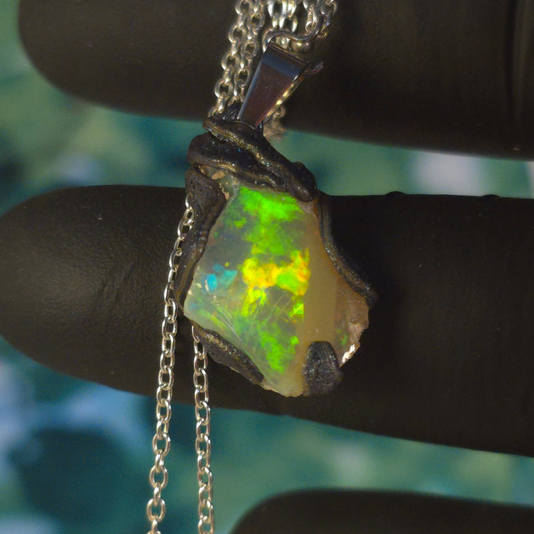 Video: raw uncut Ethiopian Welo opal pendant. Colour: blue, red, with green and yellow accents, vivid. Body: white. Held in a gloved hand against a green background.