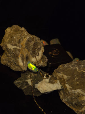 Raw uncut Ethiopian Welo opal pendant, green flashes on light blue. Resting on rough rock.
