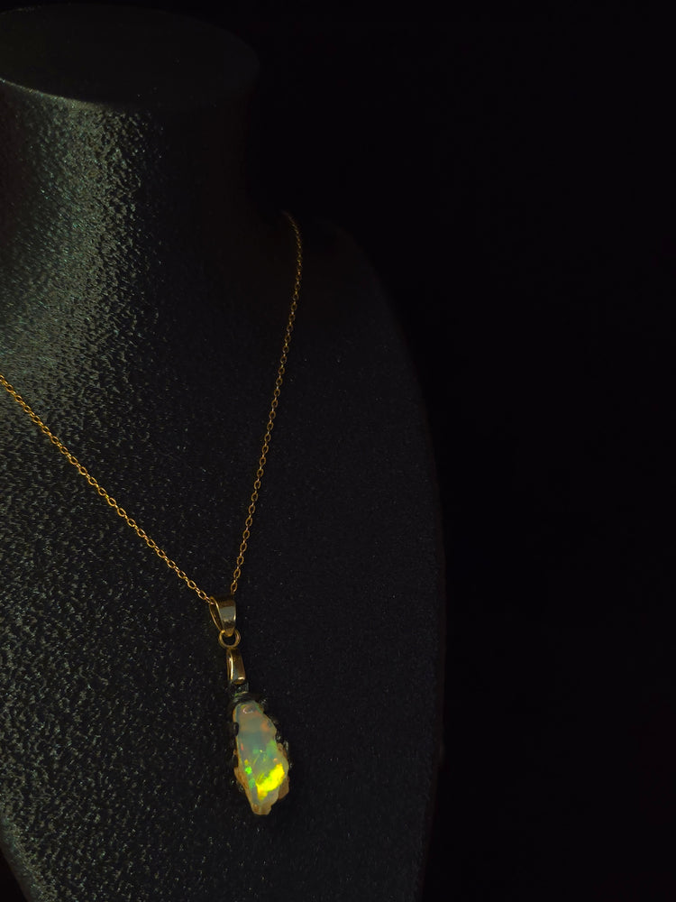 Raw uncut Ethiopian Welo opal pendant, green flashes on light blue. Worn on a black display bust.