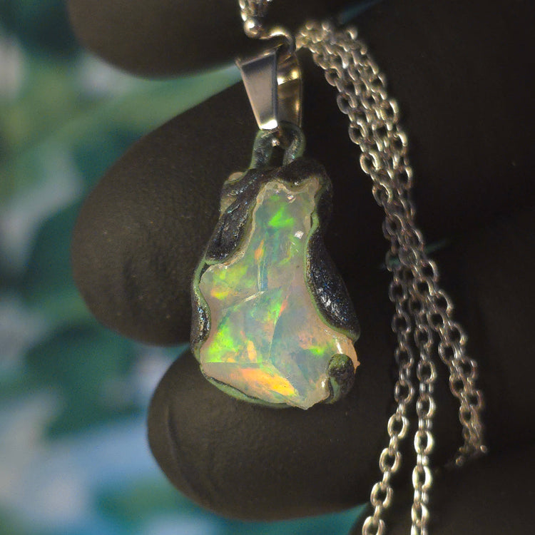 Video: raw uncut Ethiopian Welo opal pendant. Colour: green, blue-green, with red hints, vivid. Body: white. Held in a gloved hand against a green background.