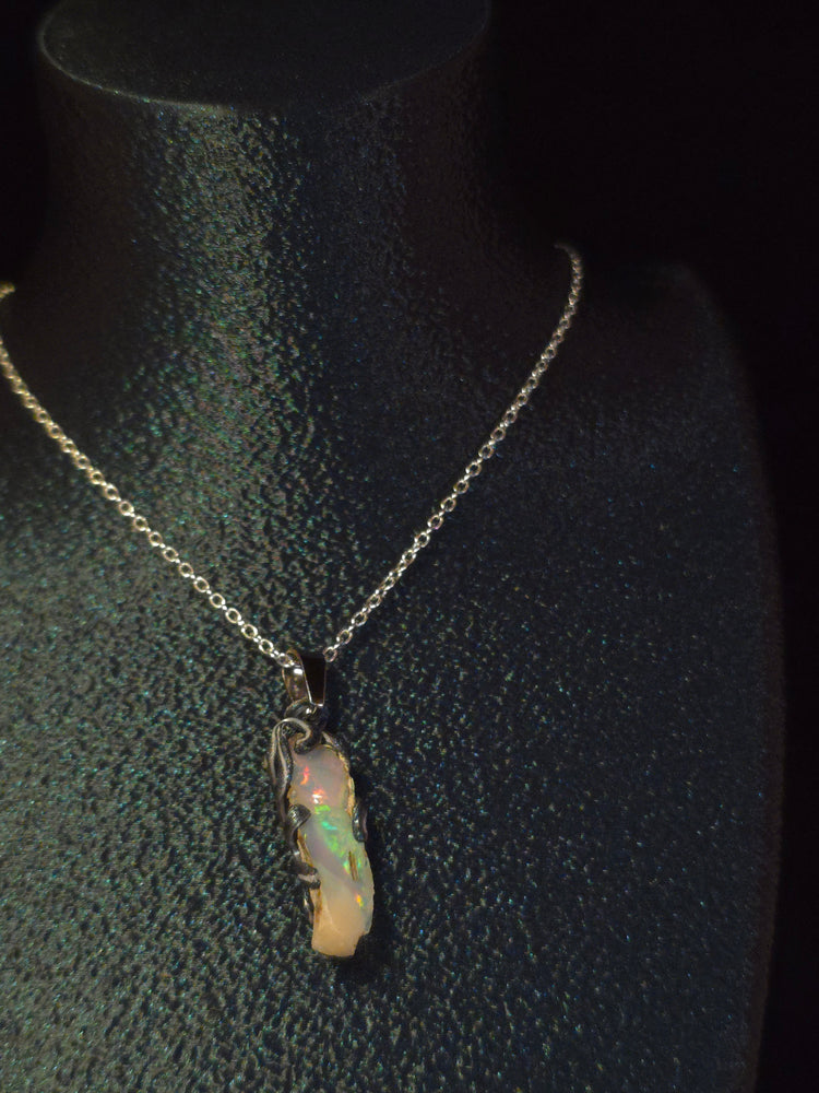 Raw uncut Ethiopian Welo opal pendant, rainbow flashes & red fire. Worn on a black display bust.