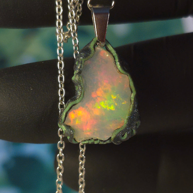 Video: raw uncut Ethiopian Welo opal pendant. Colour: full spectrum rainbow, moderate. Body: white. Held in a gloved hand against a green background.